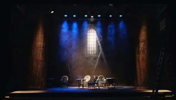 Theatre stage lit in blue, with chairs and a table set for a play