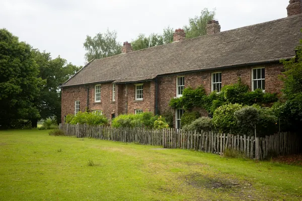 Long brick house with a tiled roof behind a picket fence and lawn