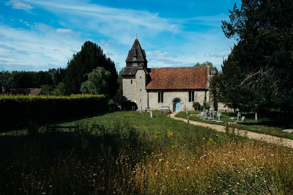 Small village church with a shingled spire among trees and long grass
