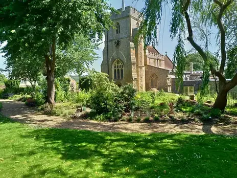 Stone church tower seen through trees across a garden