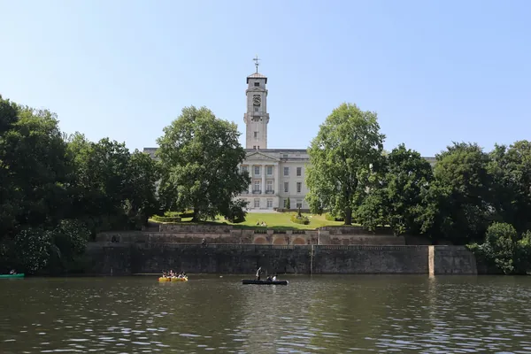Rowing boats on a park lake with trees and a building beyond