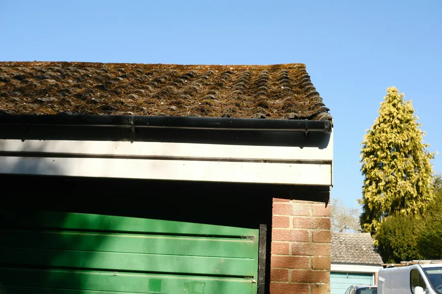 Black gutter along the eaves of a mossy tiled garage roof