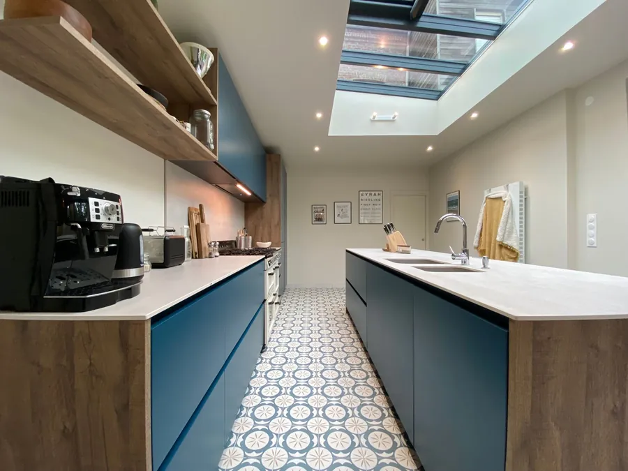 Long kitchen extension with blue units, a patterned tiled floor and a glazed roof lantern set into the flat roof