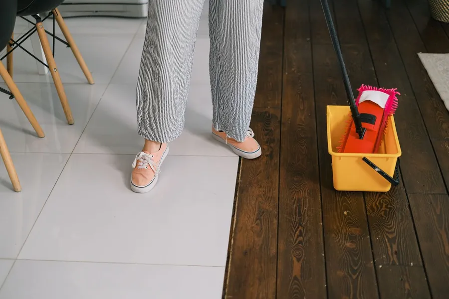 Mop and yellow bucket on a wooden floor indoors, used to soak up water while a roof leak is contained