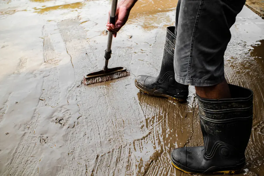 Roofer in boots brushing primer across a wet flat surface before a patch repair on a Dartford flat roof
