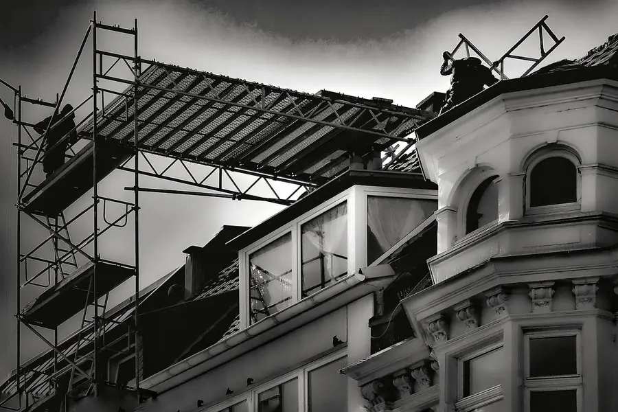Black and white view of scaffolding and a roof platform against the bay windows and eaves of a period building