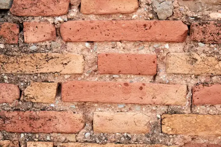Close-up of weathered red and buff bricks with crumbling, eroded mortar joints between them