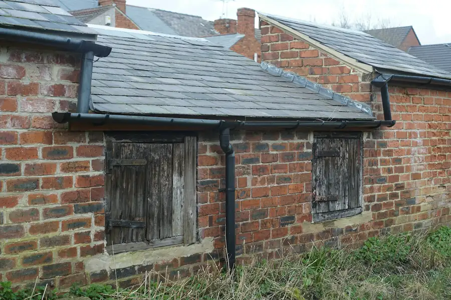 Brick outbuilding with a slate roof and gutters along the eaves