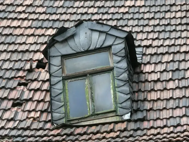Old clay-tiled roof with a cracked and slipped tile next to a lead-clad dormer