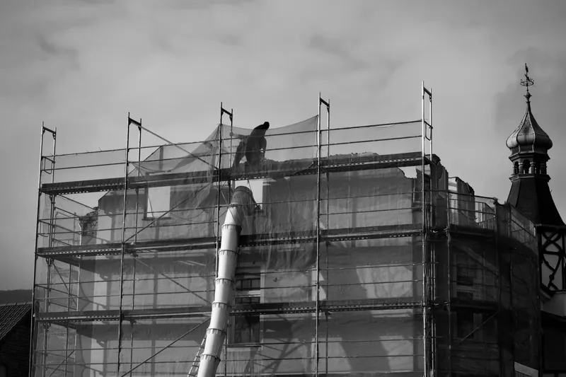 Scaffolding and netting round a building, with a waste chute down the side, during roof work