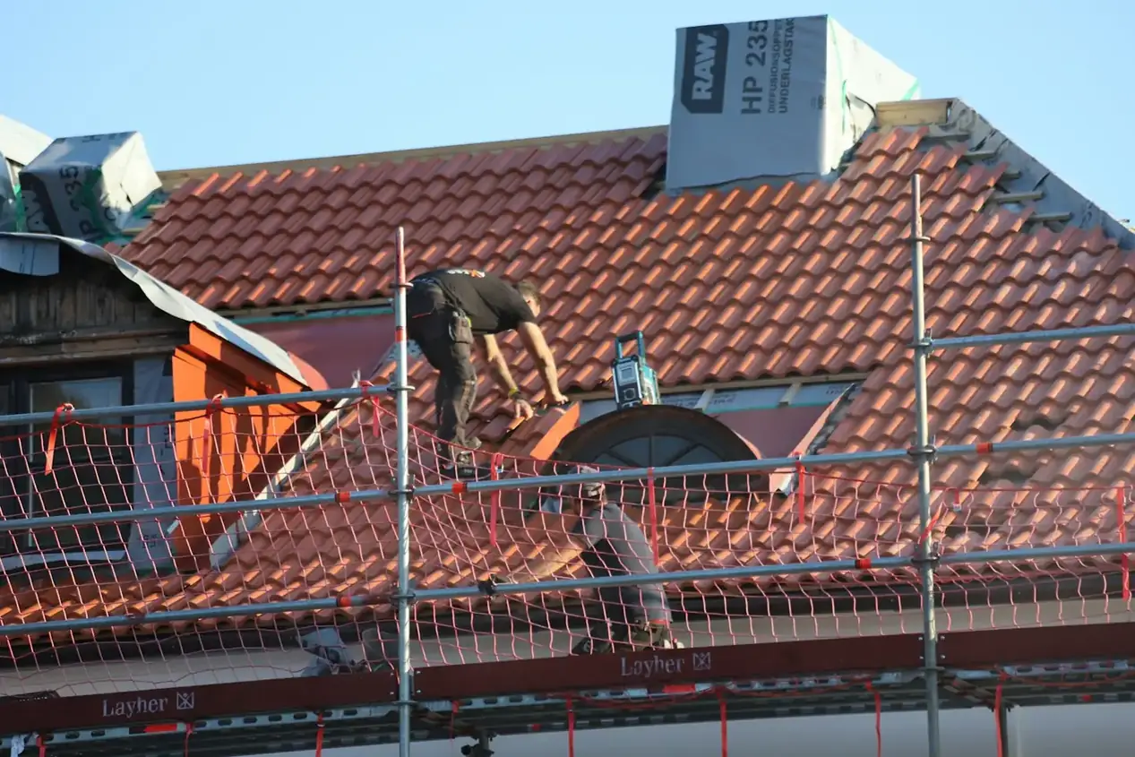 Roofer fixing new red clay tiles from a scaffold platform during a re-roof