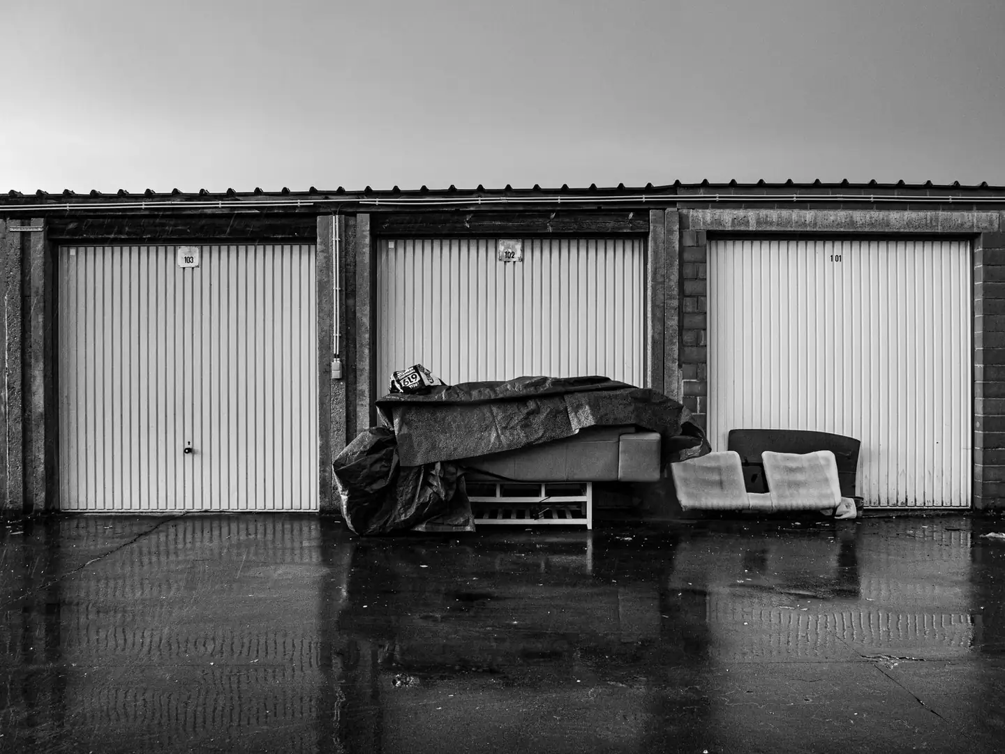 Row of lock-up garages with up-and-over doors and a flat sheet roof