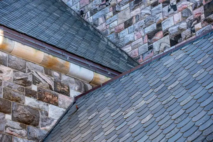 Slate roof valley meeting a stone wall, with a metal gutter along the edge