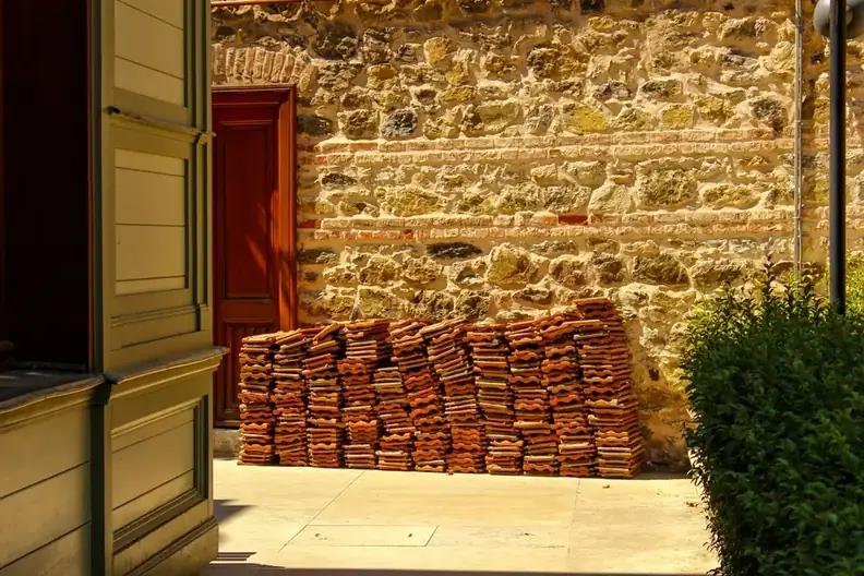Stack of reclaimed clay roof tiles set against an old stone wall
