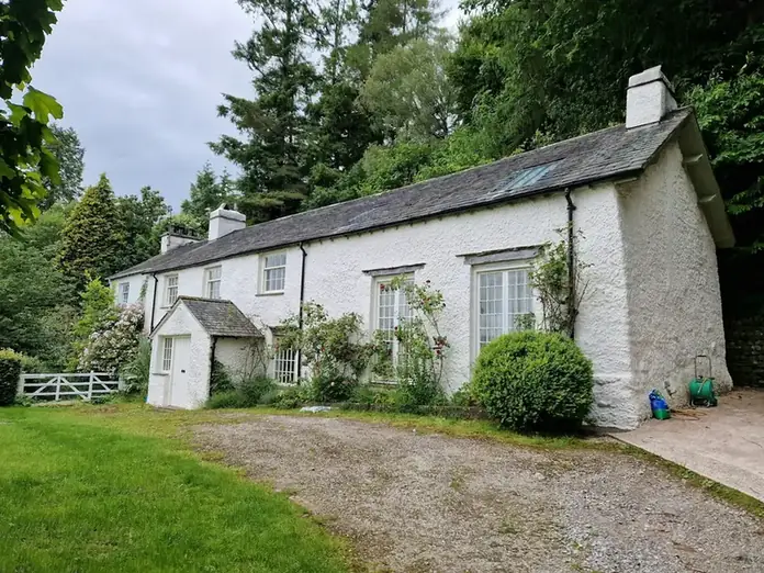 White-painted cottage with a slate roof and chimney behind a lawn