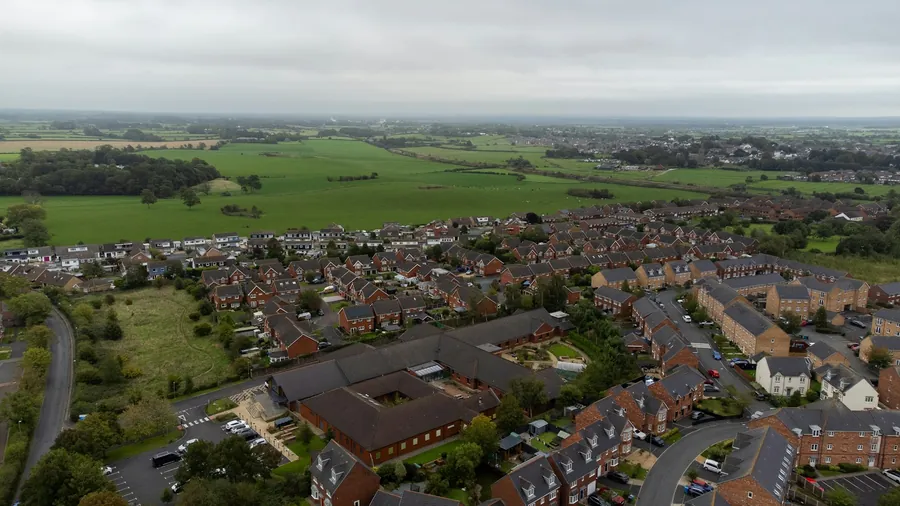 Aerial view of a brick housing estate with tiled roofs and fields beyond