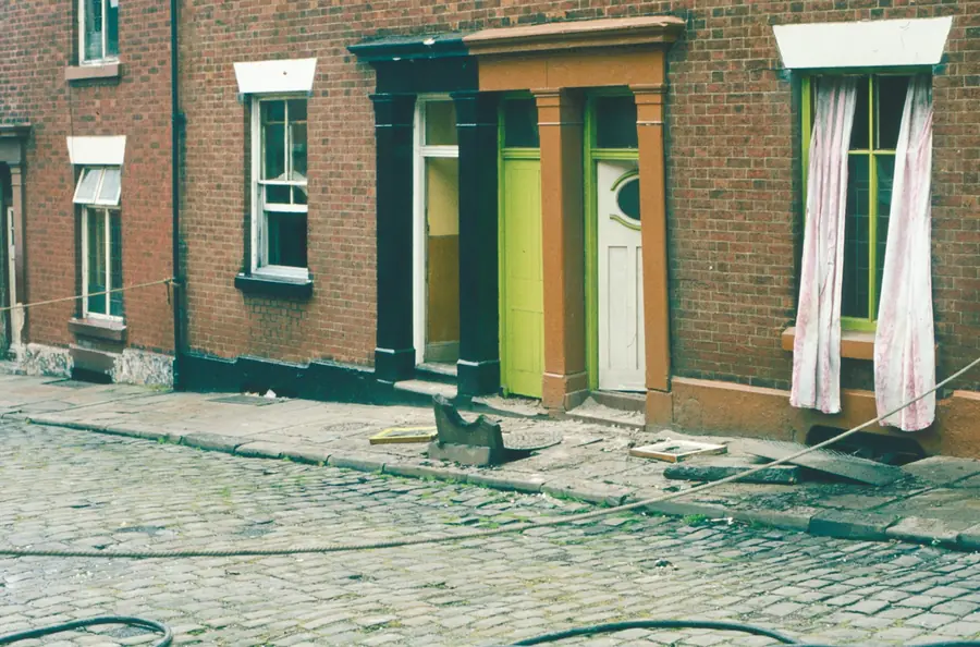 Brick terraced houses with coloured front doors along a cobbled street