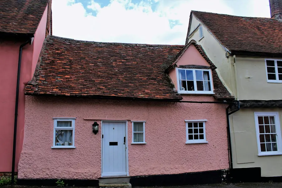 Pink-rendered cottage with a clay tile roof beside a timber-framed house